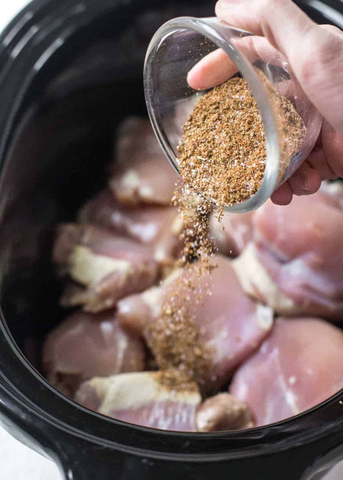 adding spices to the chicken in the slow cooker