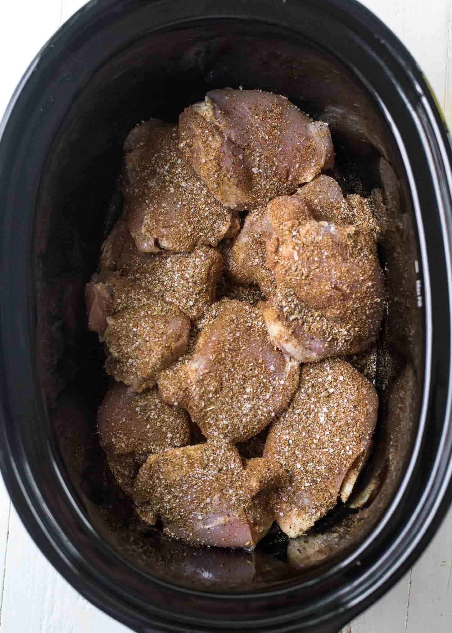 overhead image of uncooked chicken thighs covered in spices in the slow cooker