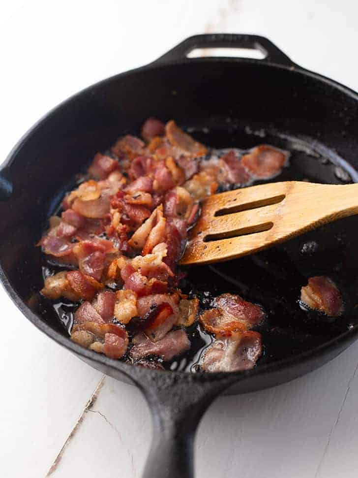 cooking bacon pieces in a cast iron skillet