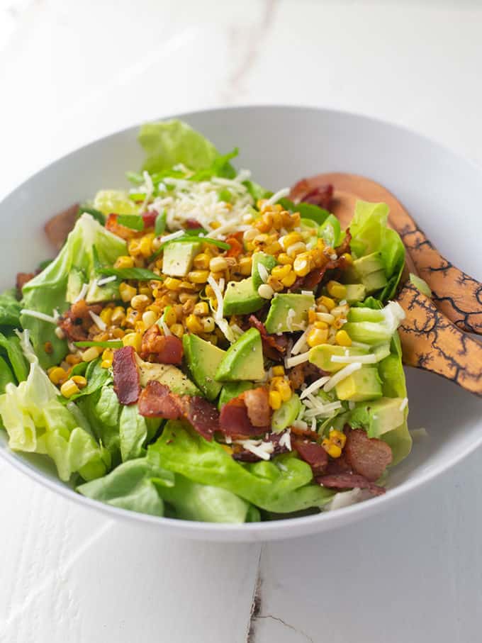 Bacon, Corn and Avocado Salad in a white bowl with salad tongs