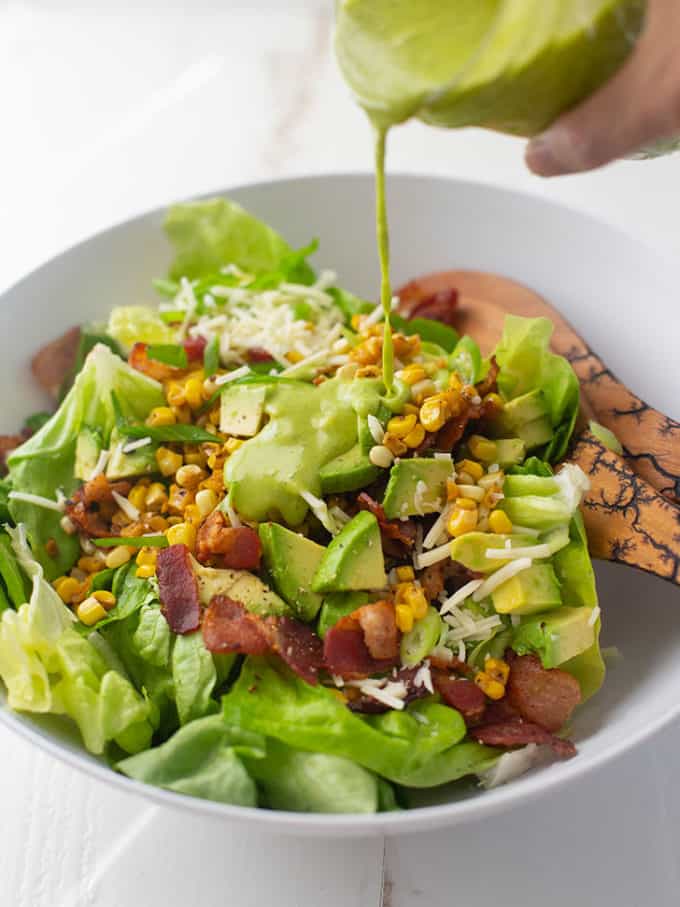 pouring dressing on bacon, corn and avocado salad