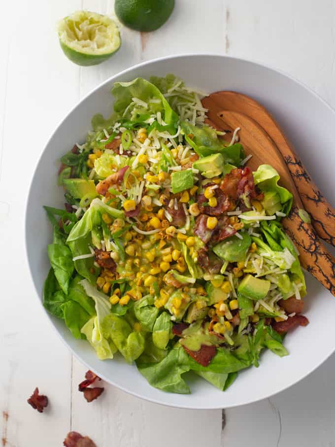 bacon, corn and avocado salad in a white bowl with salad tongs