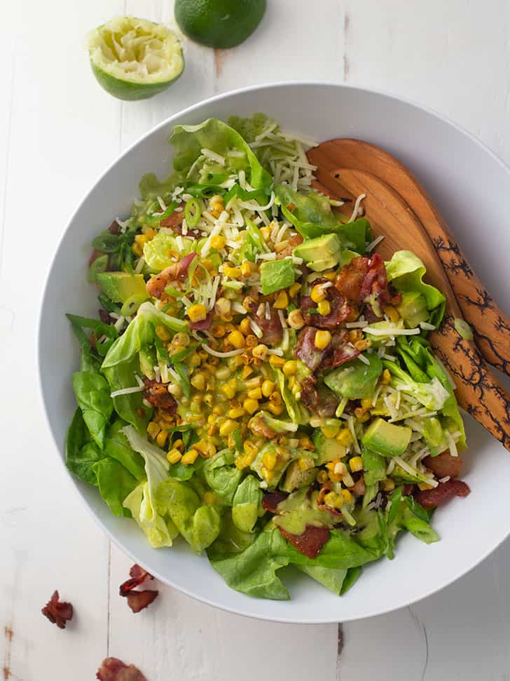 bacon, corn and avocado salad in a white bowl with wooden spoons