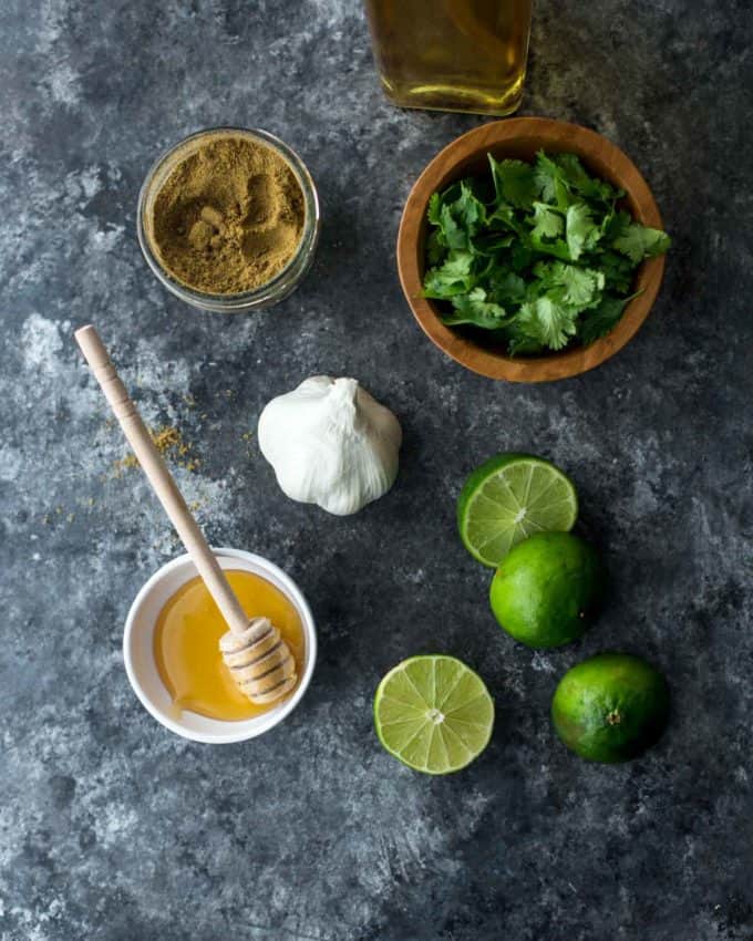 cilantro, cumin, garlic, honey, olive oil and lime in bowls on a grey background