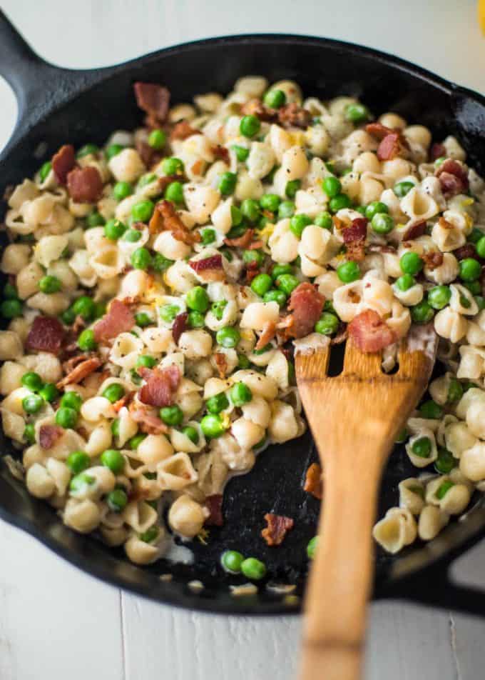 creamy shells with peas and bacon in a skillet with a wooden spoon