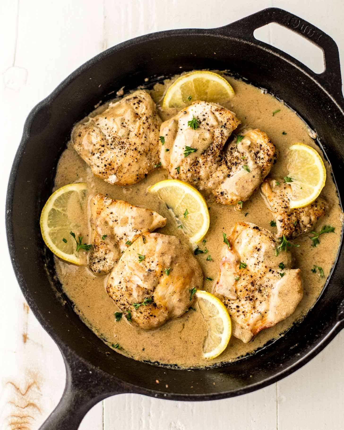 overhead image of cooked chicken thighs in a skillet on a white table