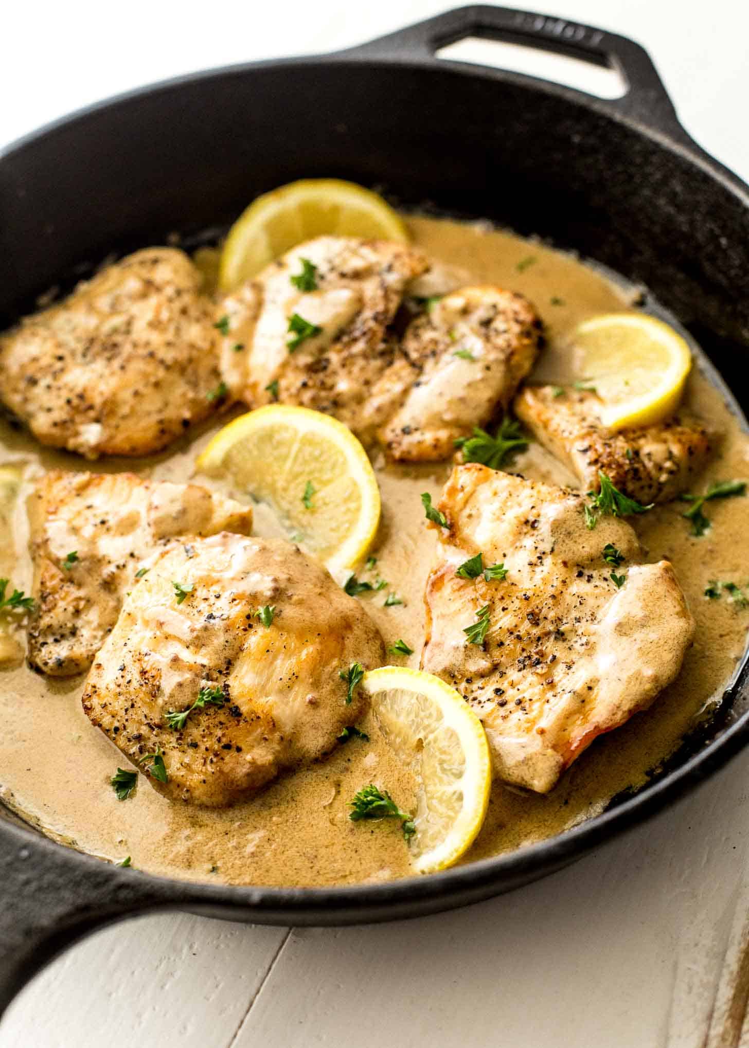 chicken thighs in creme fraiche sauce with lemon slices, all in a cast iron skillet 