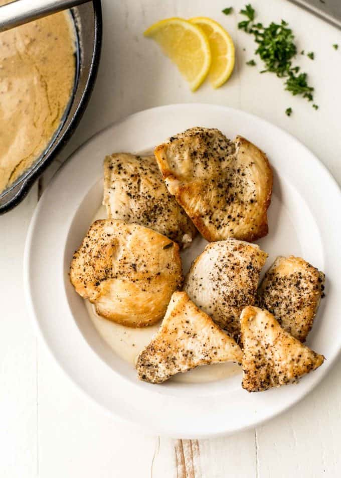 chicken breasts on a white plate next to a skillet
