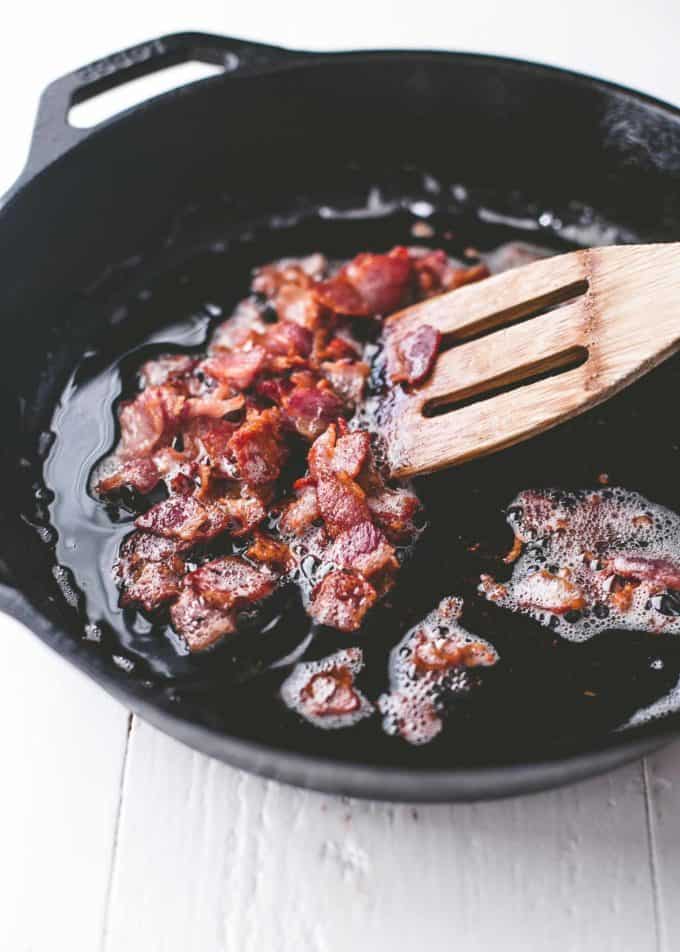 cooking bacon pieces in a cast iron skillet 
