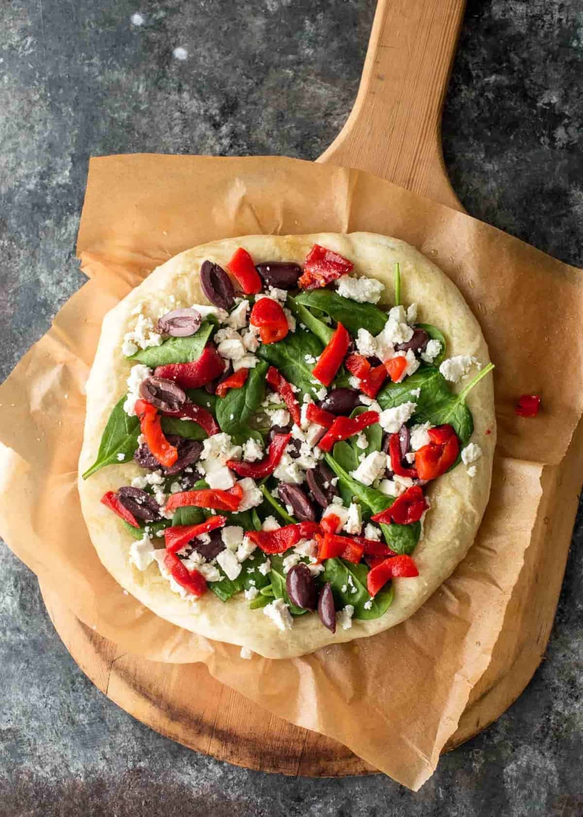 unbaked Greek Pizza on parchment paper