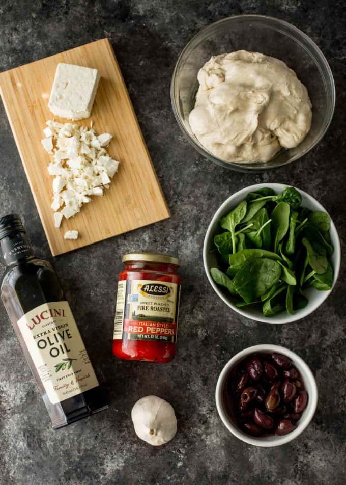 Greek Pizza ingredients: pizza dough, red peppers, olive oil, garlic, baby spinach, olives and feta