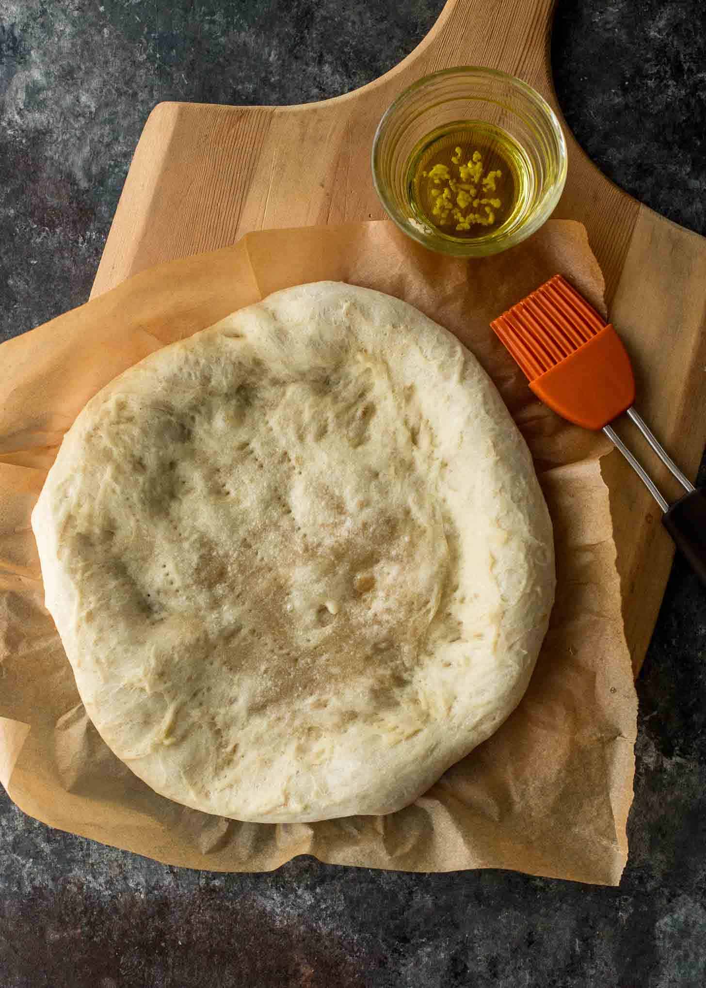 overhead image of pizza dough on a cutting board with a pastry brush and olive oil