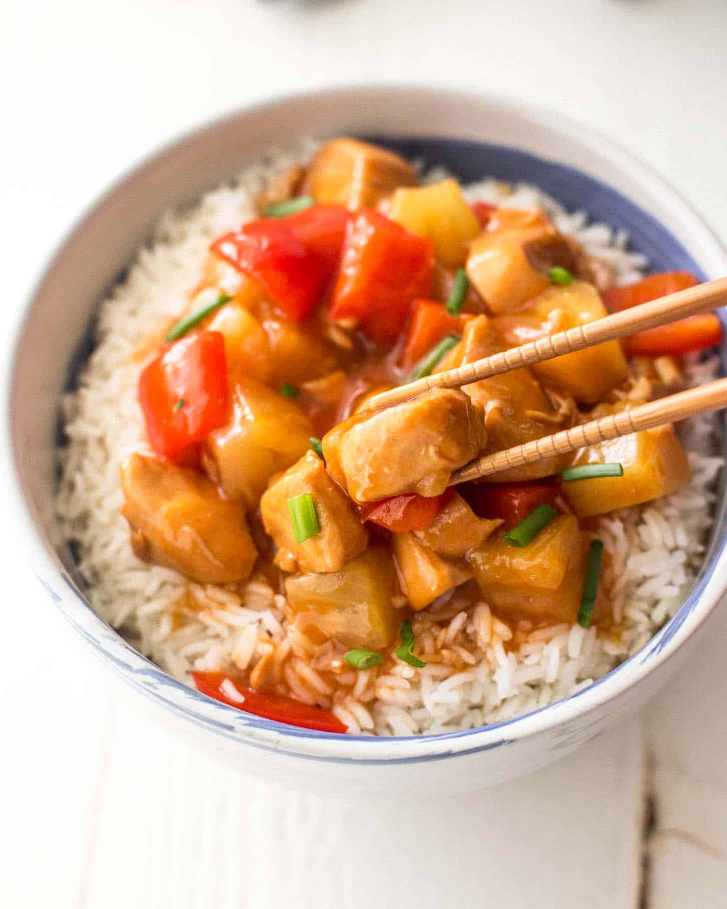 overhead image of sweet and sour chicken over rice in a bowl with chopsticks