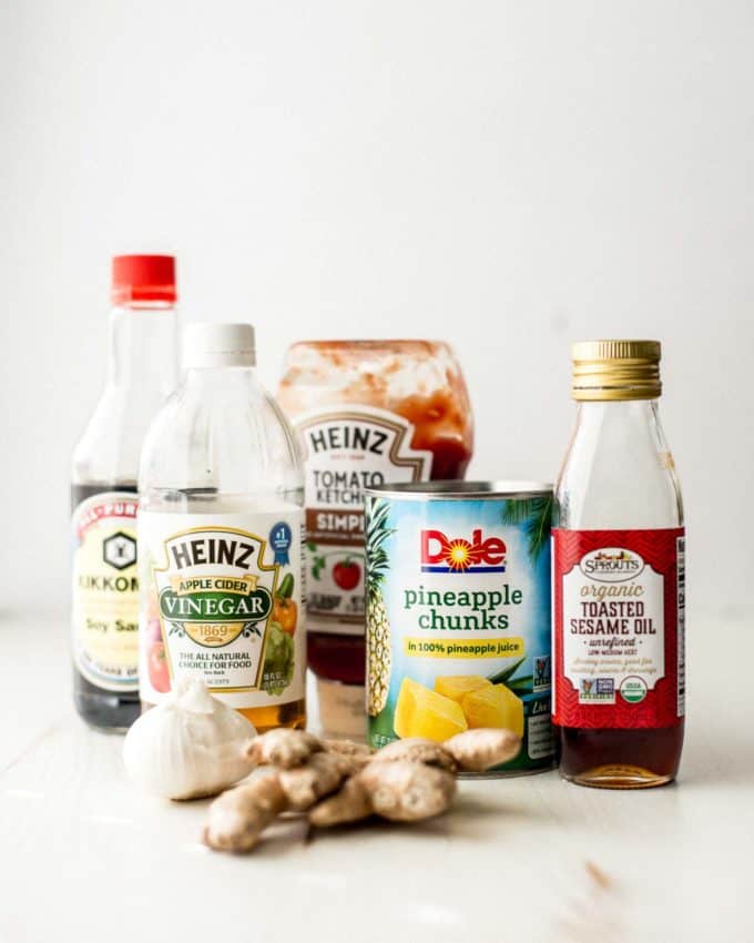 soy sauce, vinegar, pineapple chunks, ketchup, sesame oil, garlic, and ginger on a white table
