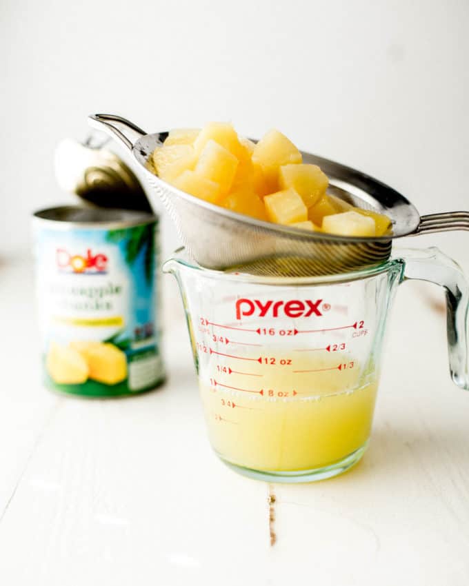 canned pineapple draining into a glass measuring jar
