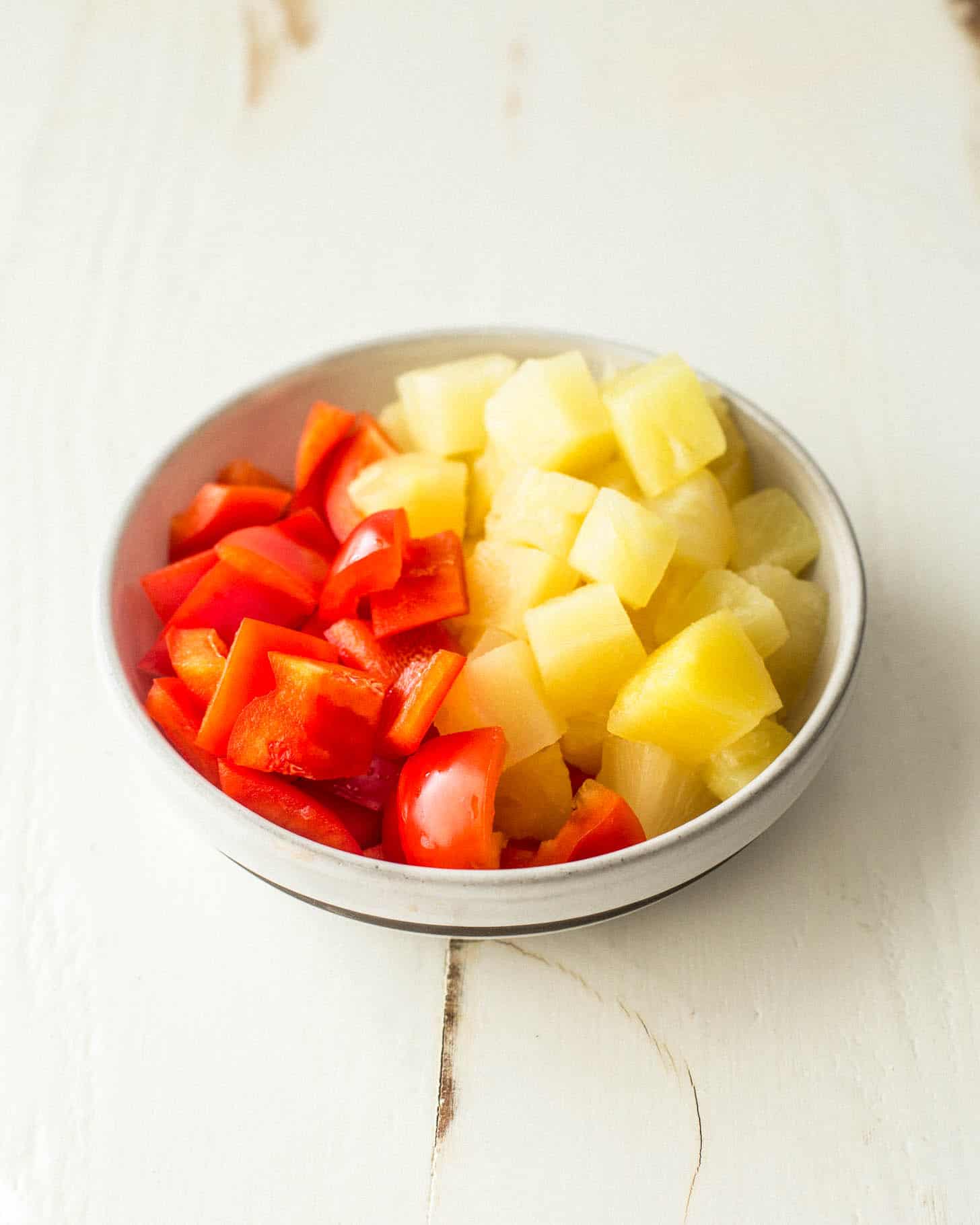 pineapple chunks and red bell pepper pieces in a small white bowl