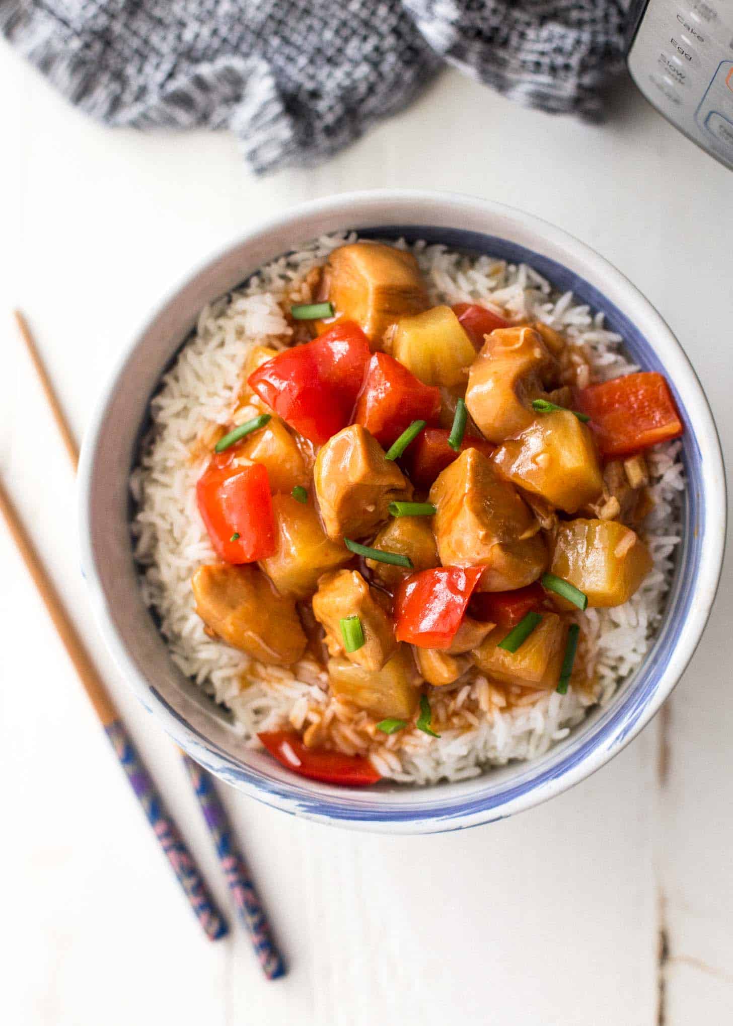 overhead image of Instant Pot Sweet and Sour Chicken over rice in a bowl, next to chopsticks on a white table