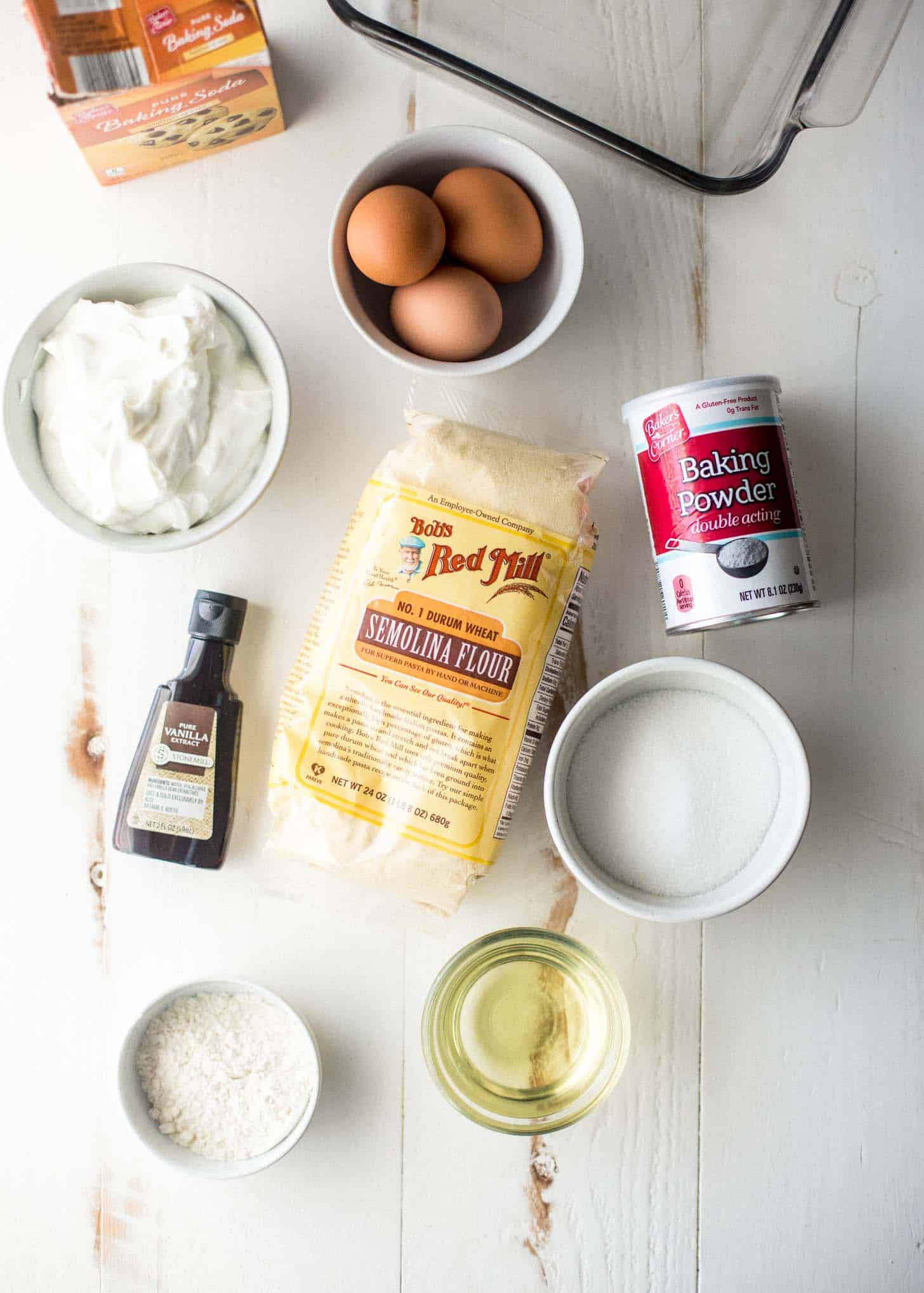 eggs, semolina flour, baking powder, vanilla, oil, sugar, and salt on a white table