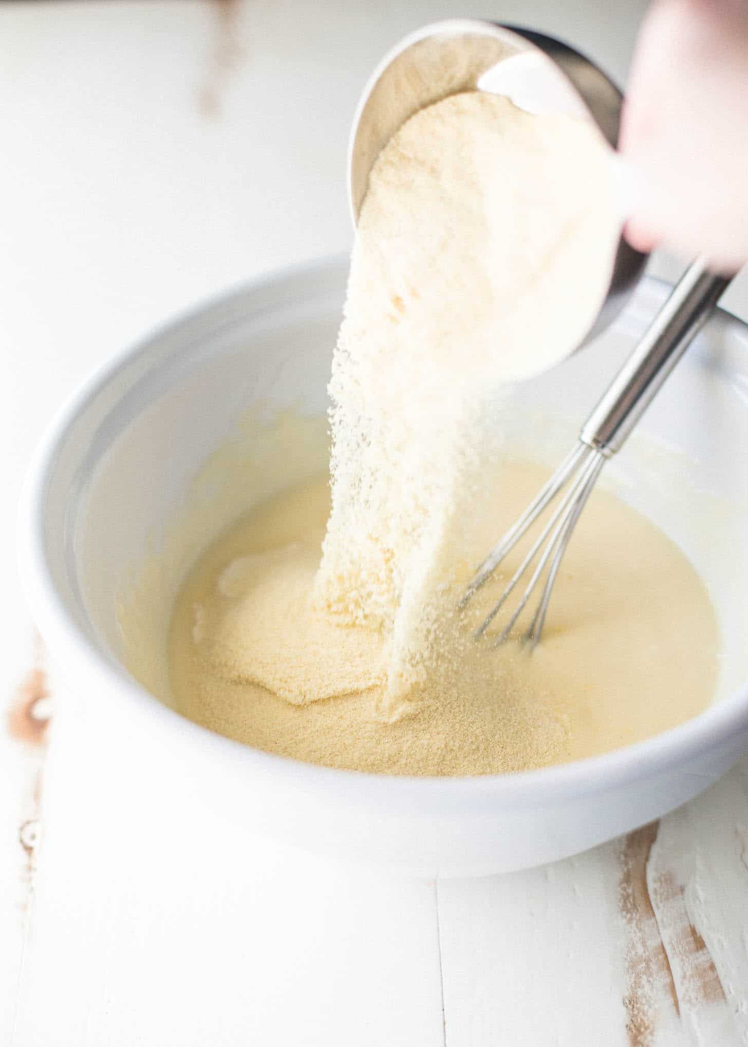 pouring semolina into cake batter in a white bowl