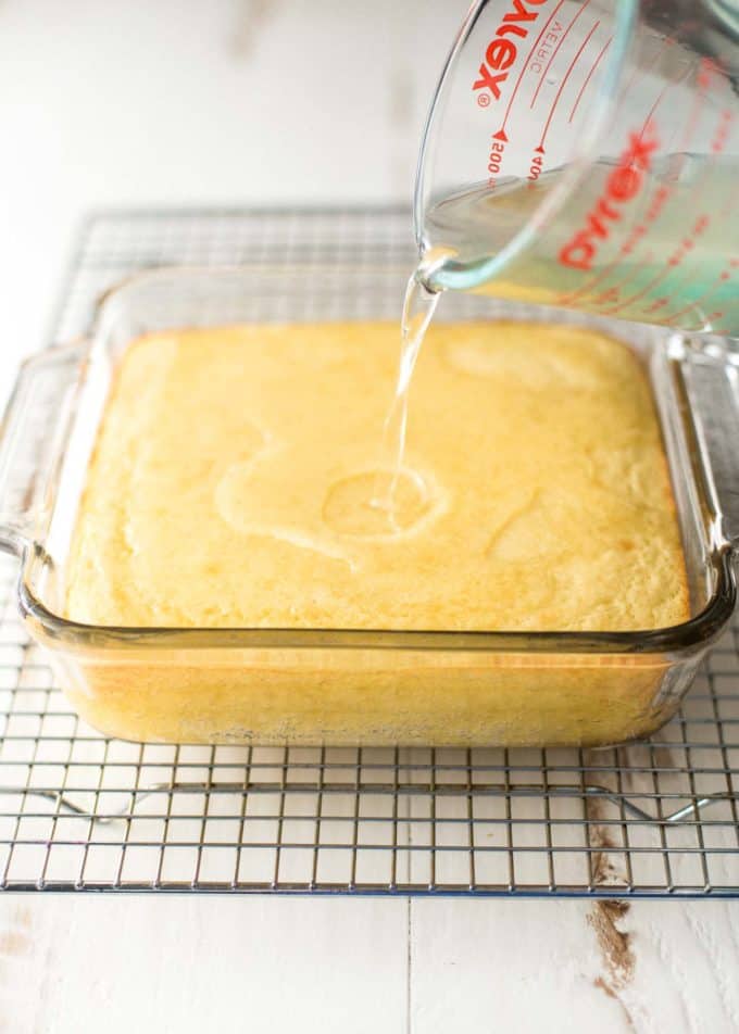 pouring simple syrup from a glass measuring cup over the baked cake 