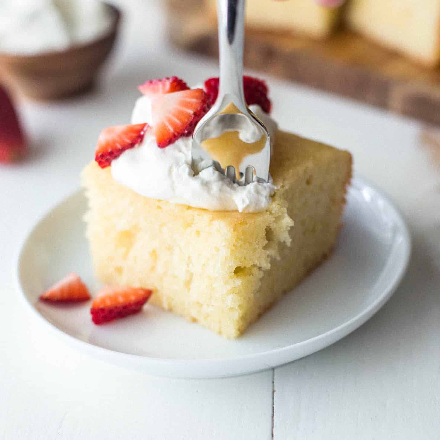 a piece of semolina yogurt cake topped with whipped cream and strawberries with a fork in it
