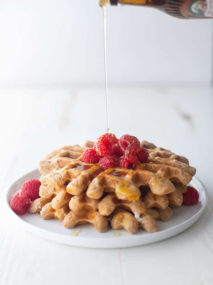 pouring syrup on whole wheat waffles topped with raspberries