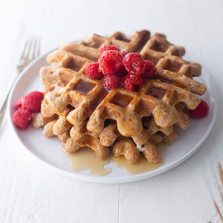 overnight yeasted whole wheat waffles on a white plate, topped with syrup and raspberries