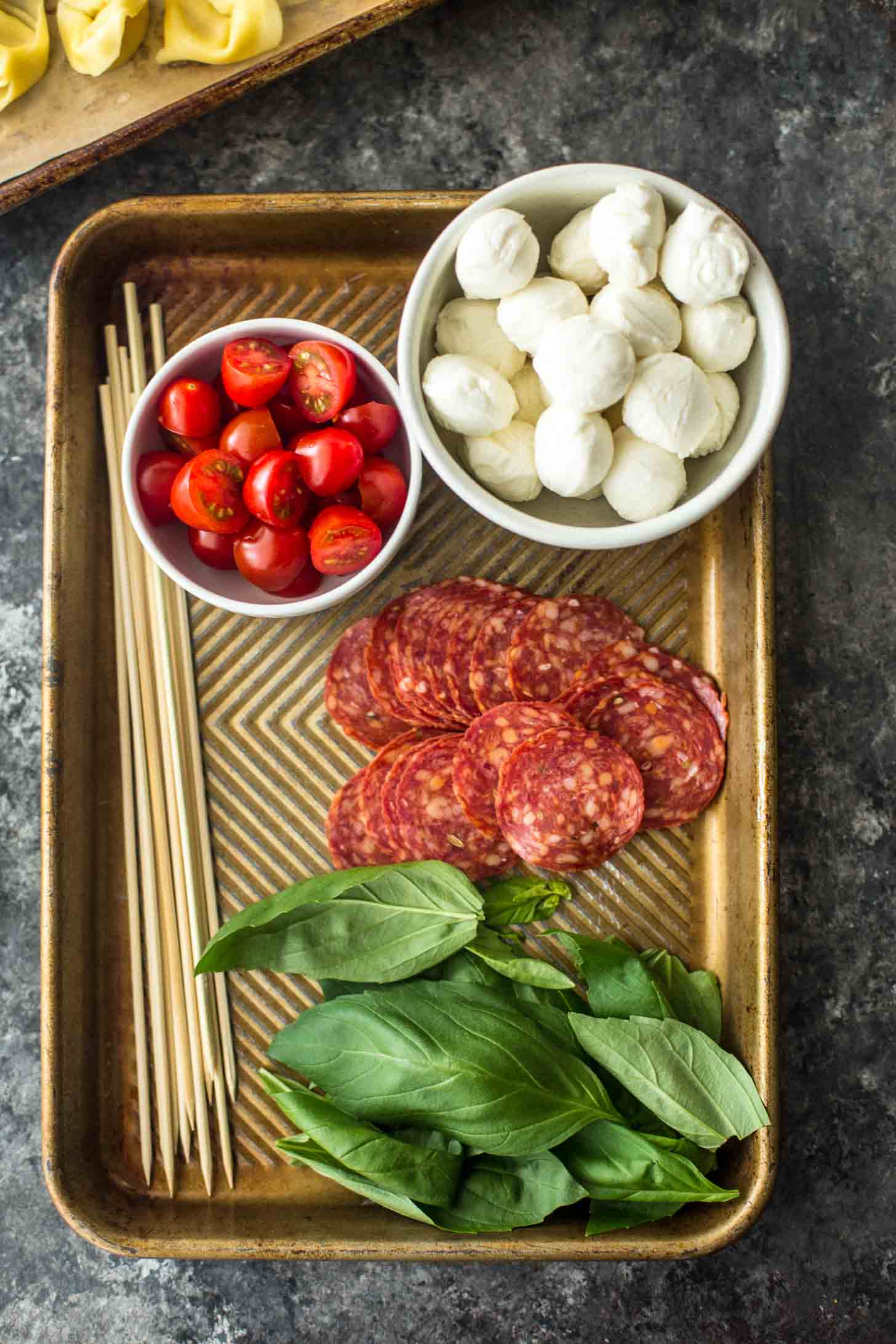 overhead image of ingredients for pasta salad skewers, including mozzarella pearls, basil, cherry tomatoes and pepperoni