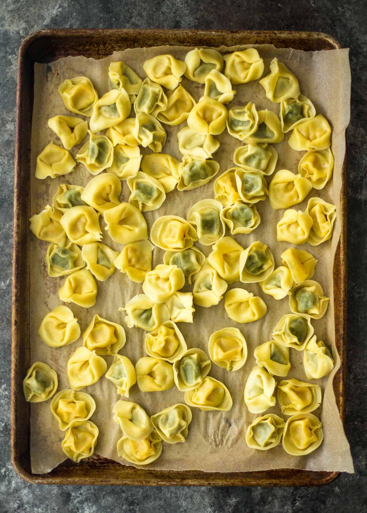 overhead image of cooling tortellini on parchment lined sheet pan