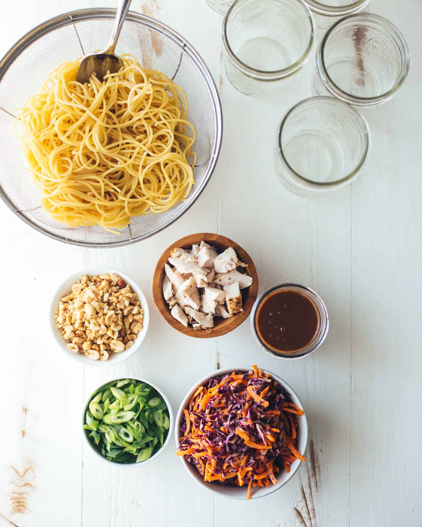 Ingredients for Sesame Noodle Salad including noodles, peanuts, chicken, carrots, cabbage and green onions on a white table top