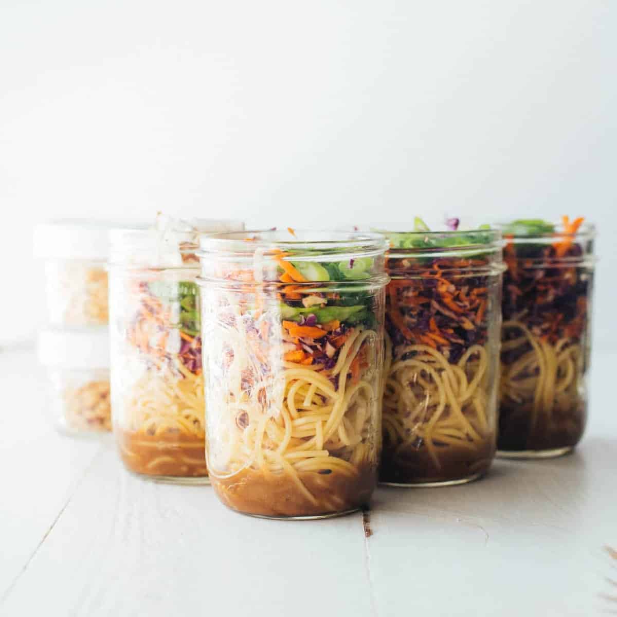 6 jars of sesame noodle salad on a white table