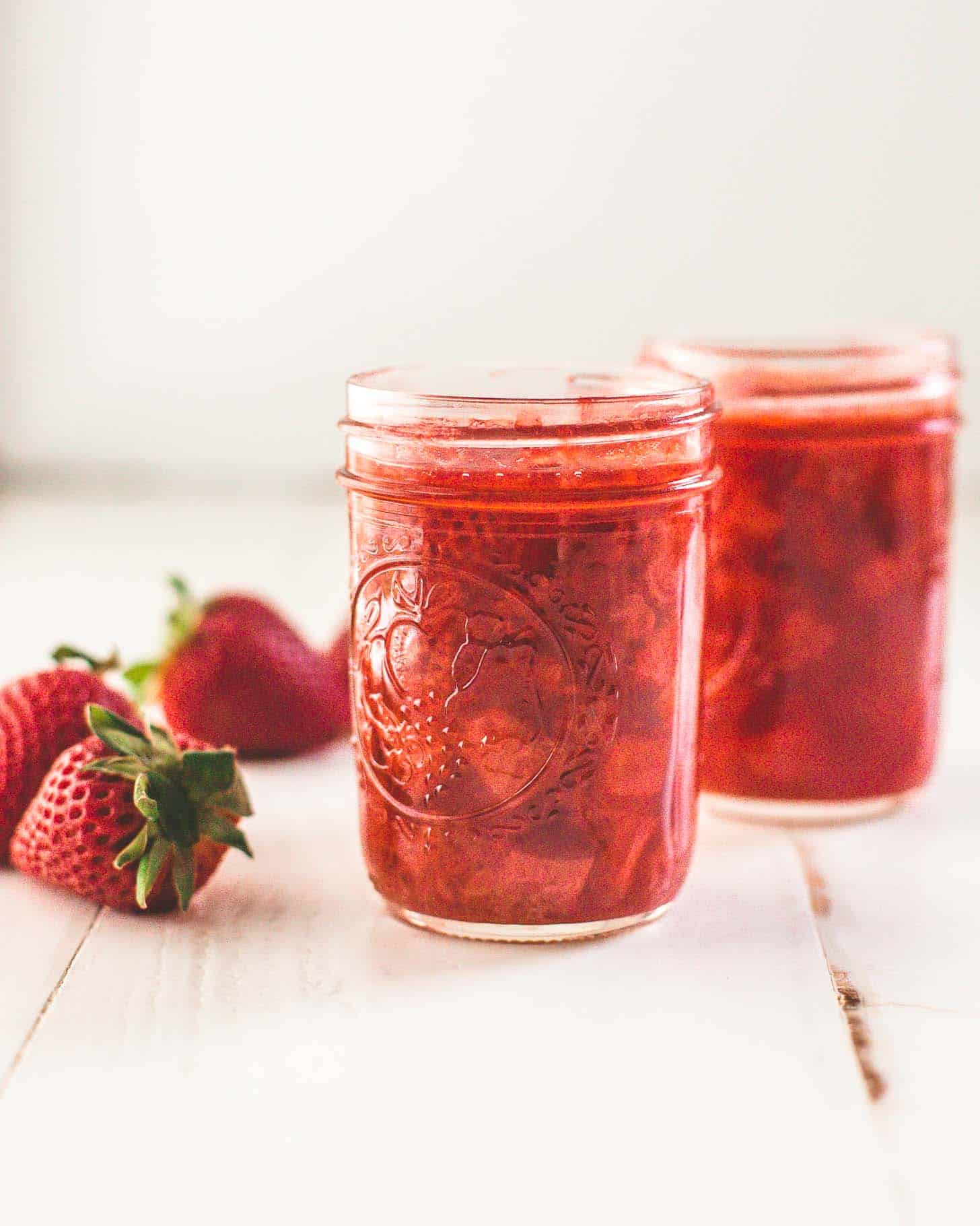 homemade strawberry syrup in small glass jars on a white tabletop