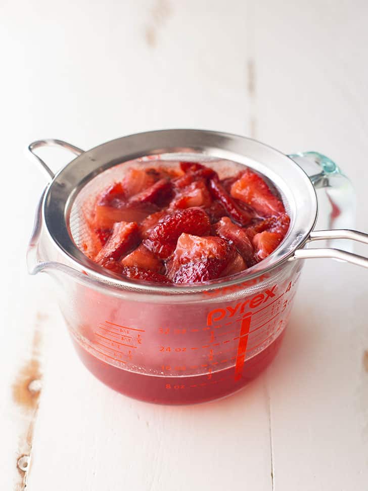 straining strawberries into a large glass measuring cup