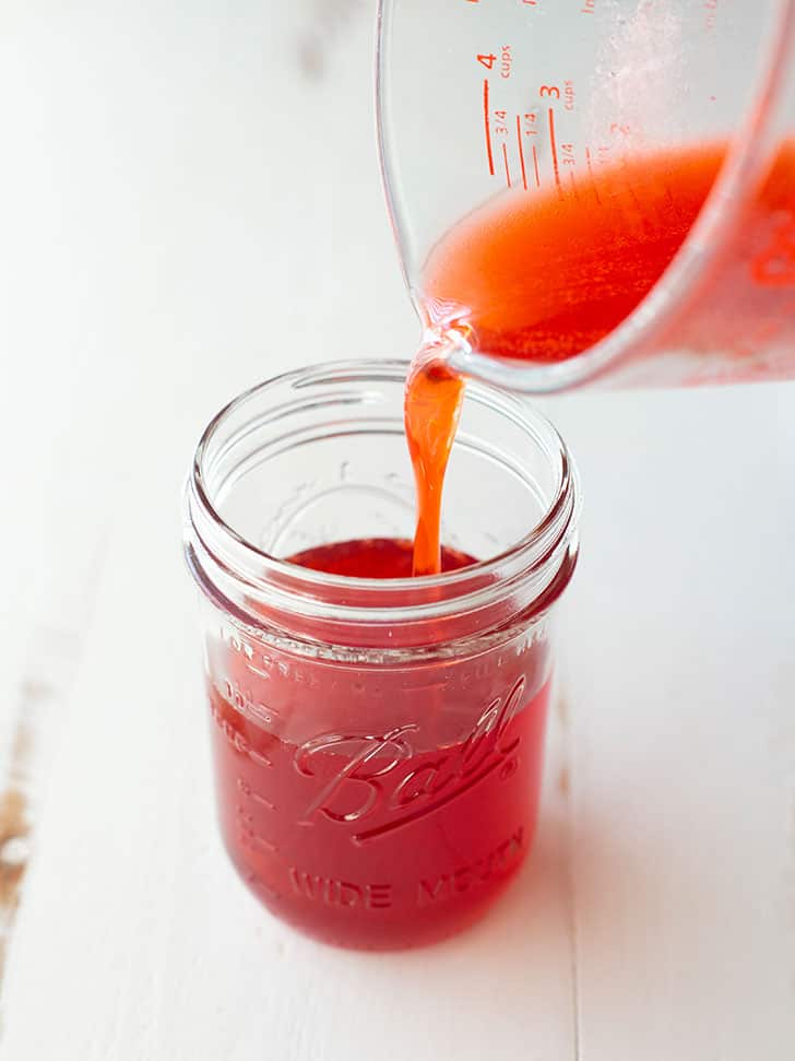 pouring homemade strawberry syrup into a small glass jar