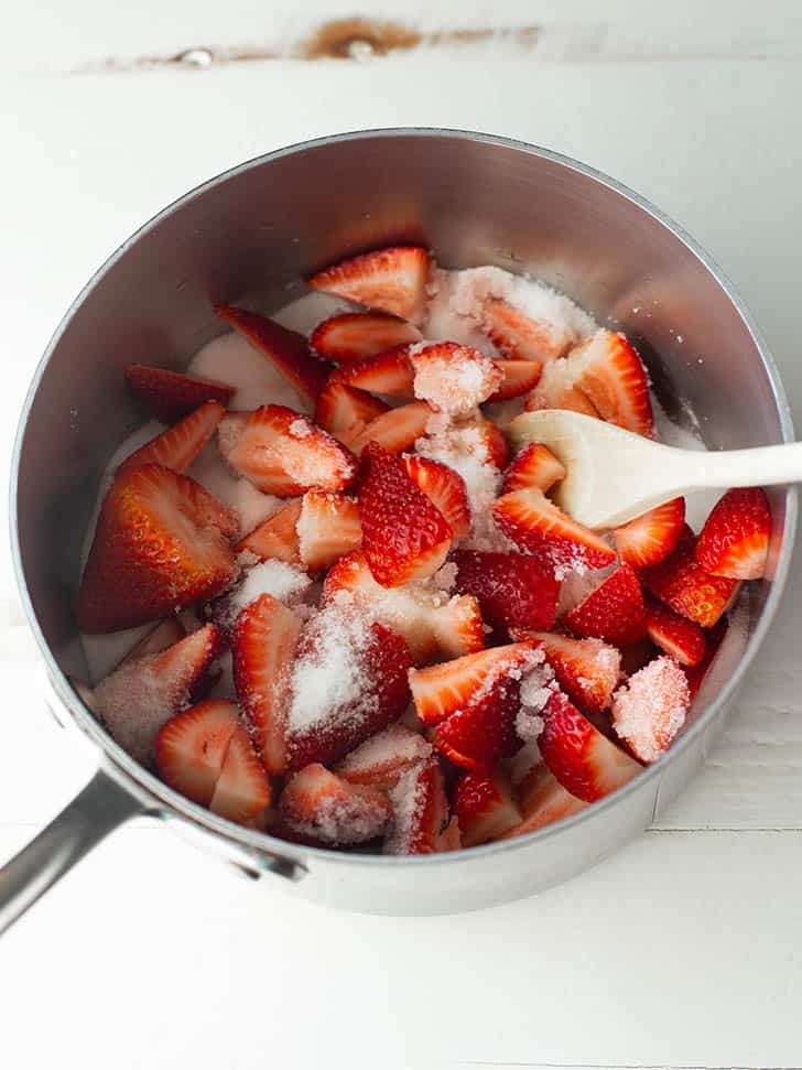 overhead image of cut strawberries in a pot with sugar