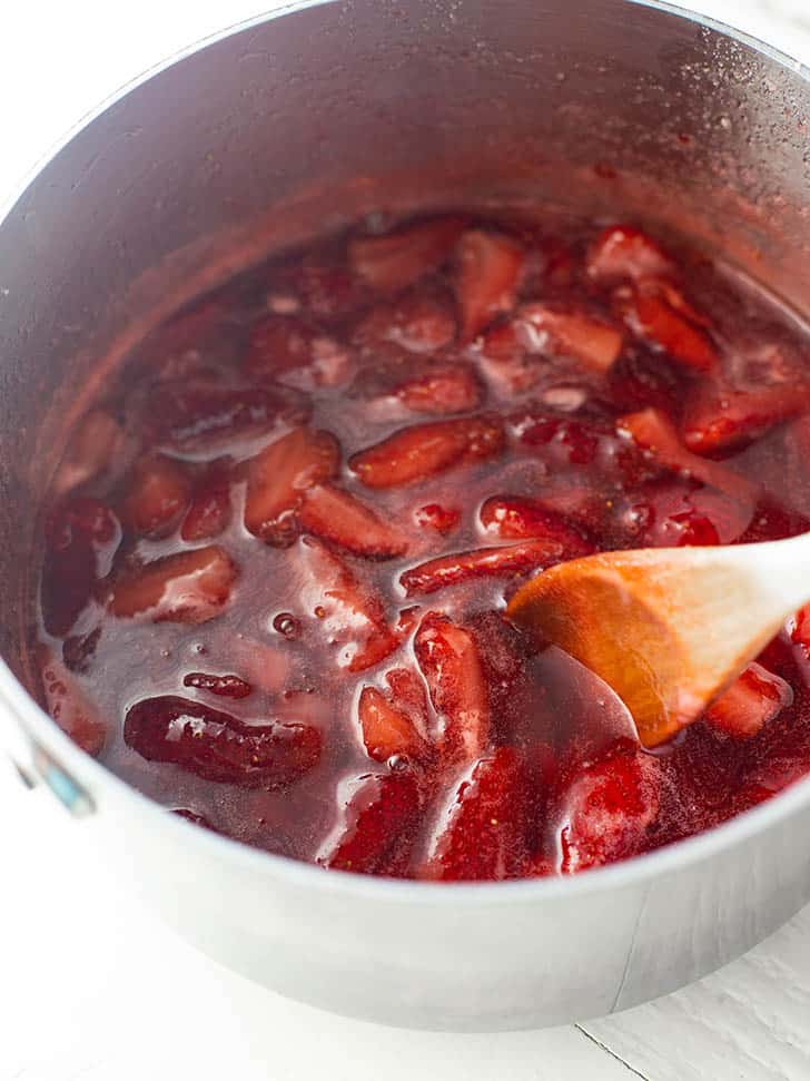 overhead image of a wooden spoon stirring strawberries in a saucepan