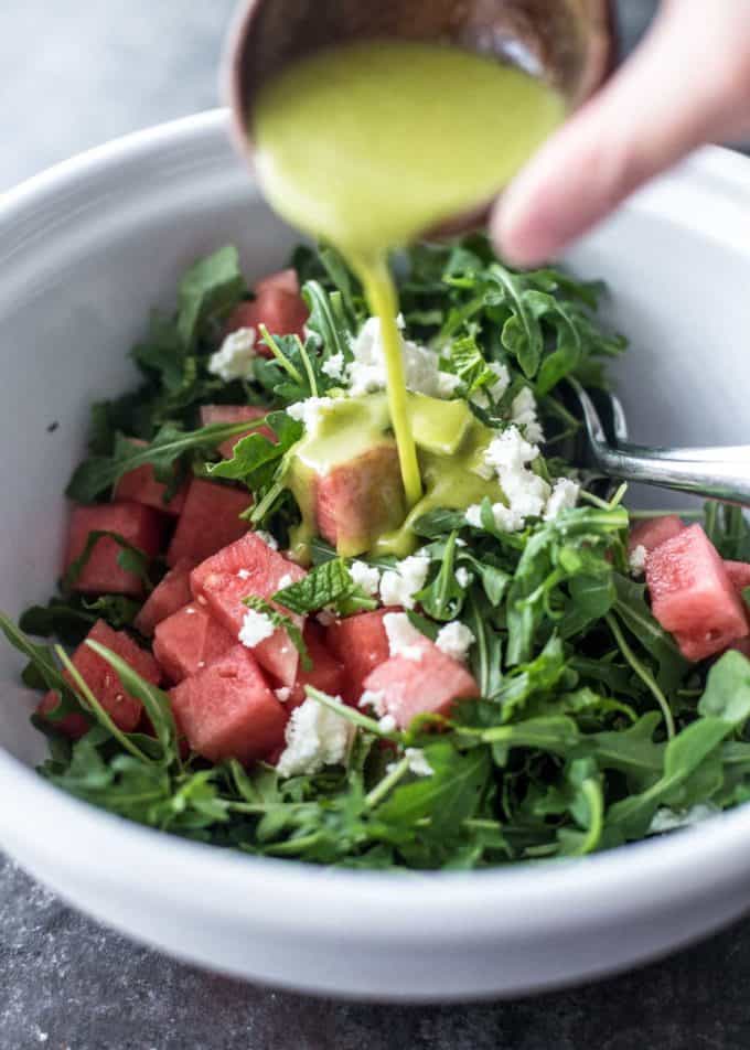 pouring sweet basil vinaigrette over the salad in a white bowl