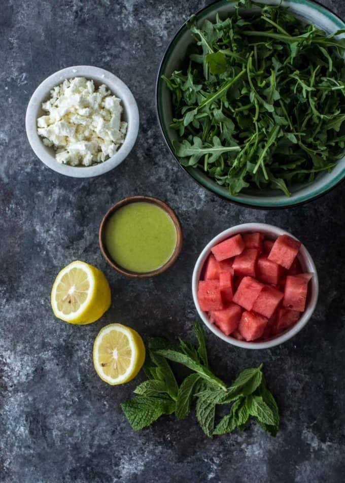 watermelon, fet, arugula, sweet basil dressing, lemon and basil on a grey table