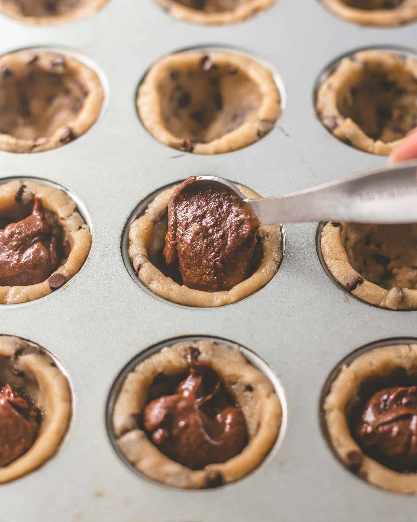 putting brownie batter into cookie dough in a muffin tin