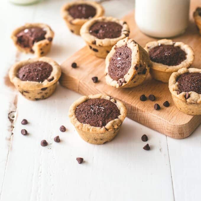 Chocolate chip brownie tarts on a wood cutting board with a glass of milk