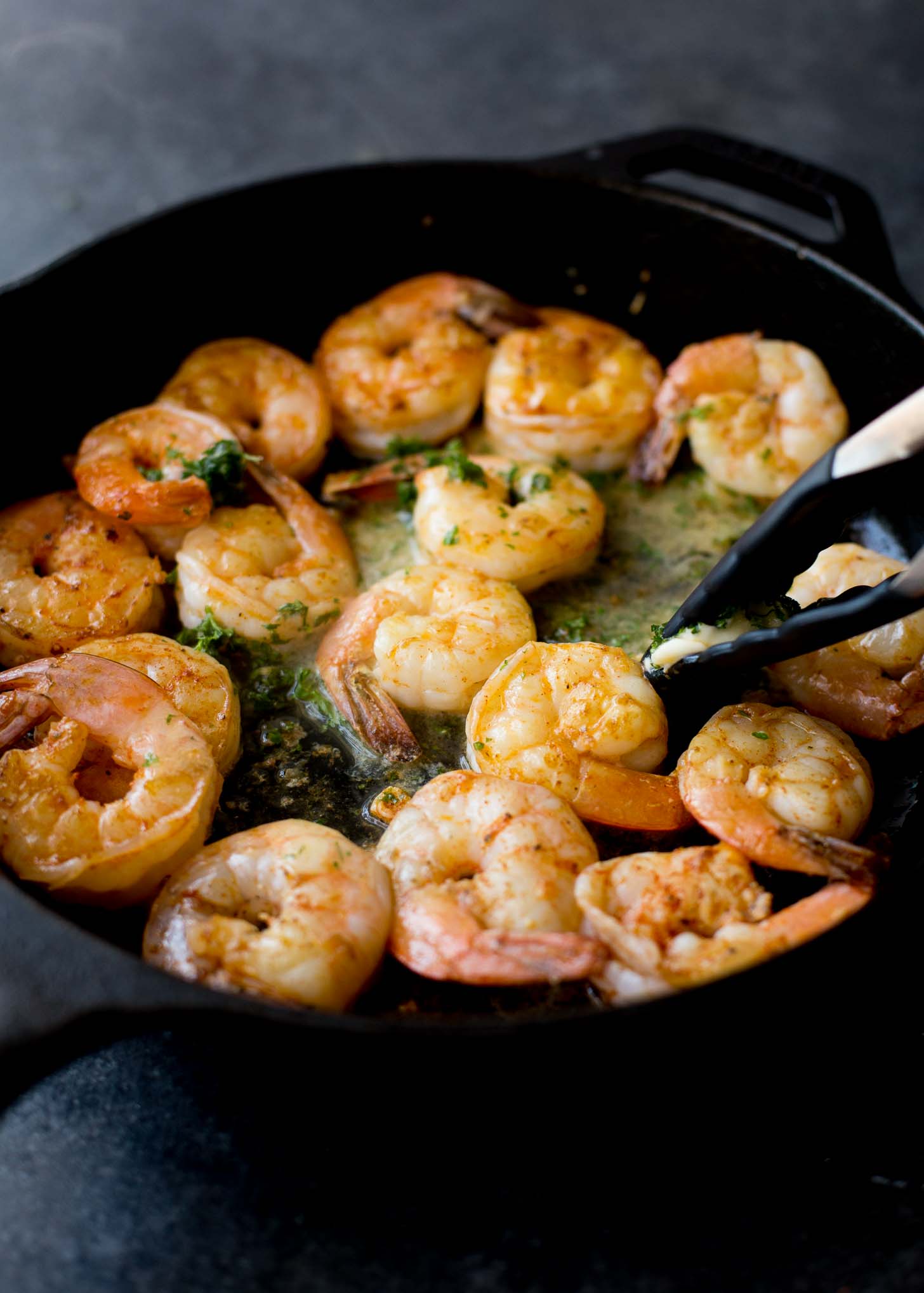 using tongs to turn shrimp in a cast iron skillet