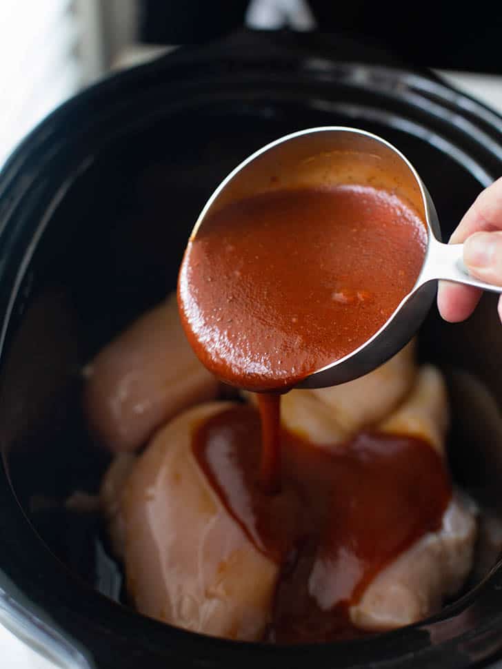 pouring barbecue sauce over chicken in a slow cooker