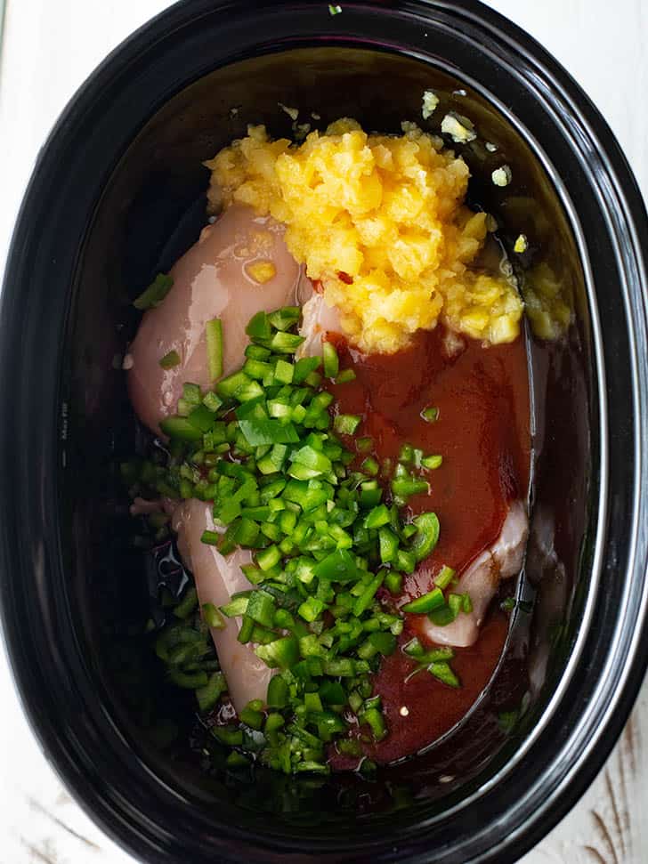 overhead image of chicken, bbq sauce, green peppers and pineapple in a slow cooker