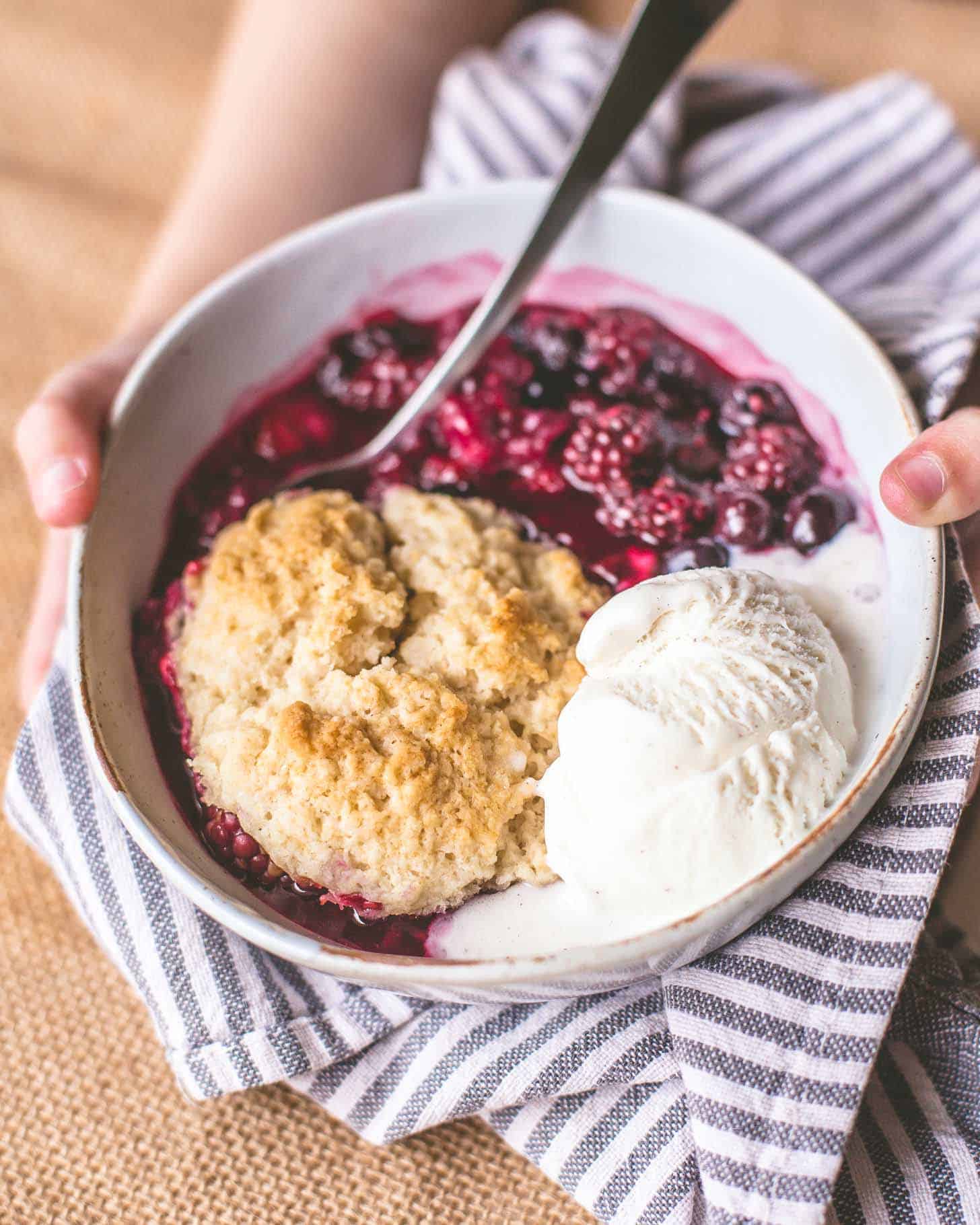hands holding a bowl of berry cobbler with ice cream