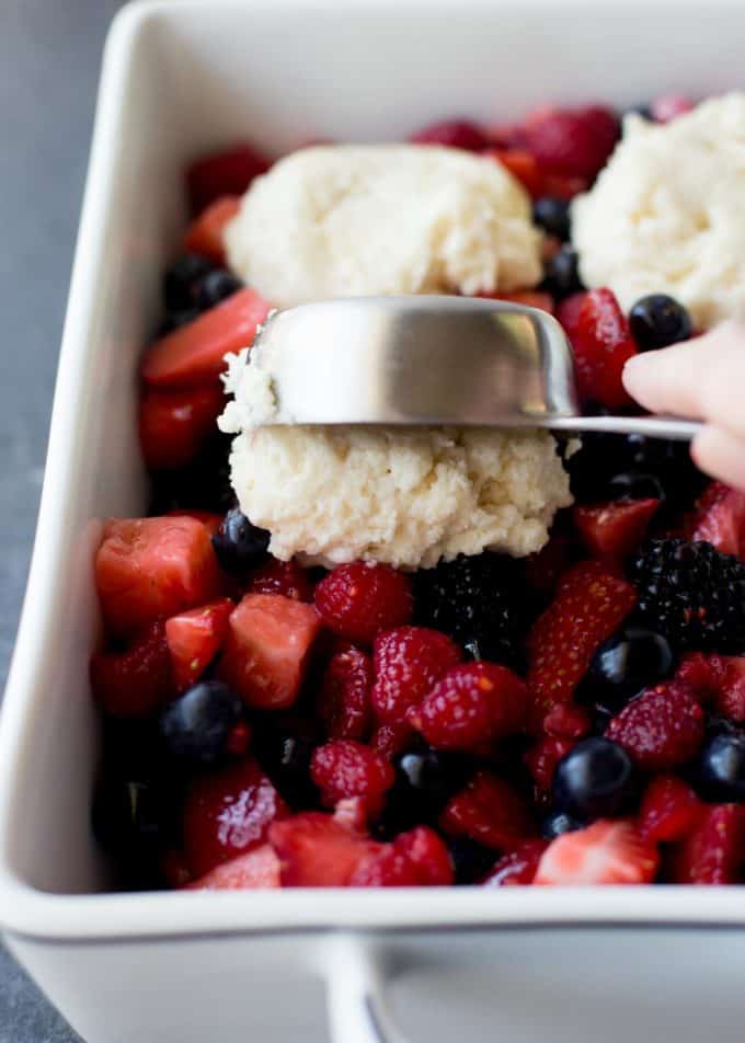 adding biscuits to berry cobbler in a white baking dish
