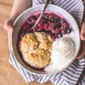 hands holding a bowl of berry cobbler with ice cream