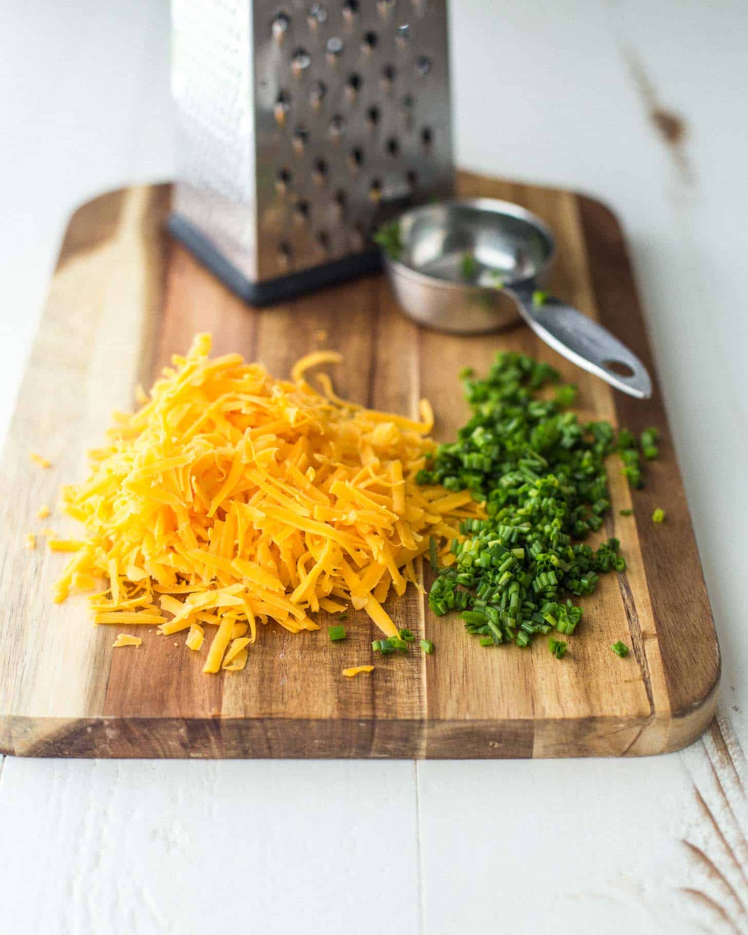 grated cheddar and chives on a wooden cutting board