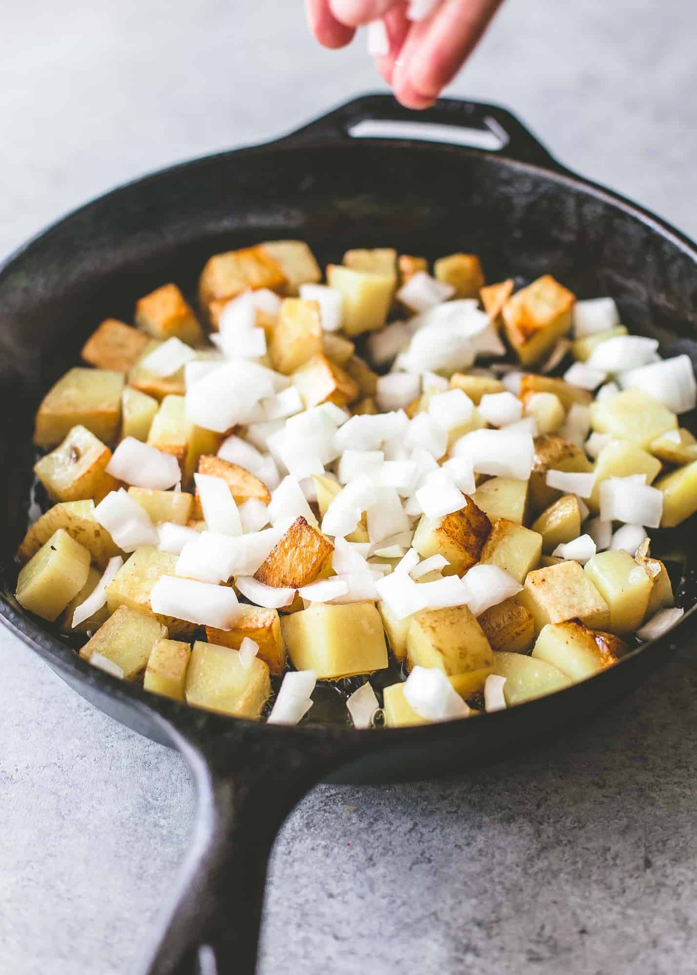 adding potatoes and onions to a cast iron skillet