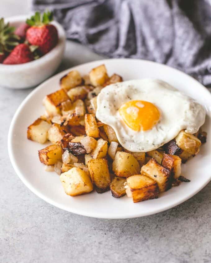 skillet home fries on a white plate topped with a fried egg