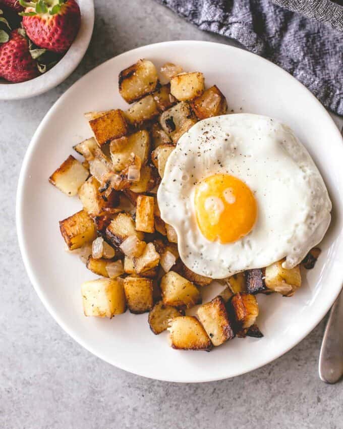 home fries on a white plate topped with a fried egg